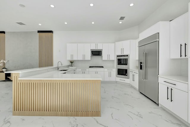 kitchen with light countertops, white cabinetry, a sink, built in appliances, and a peninsula