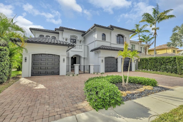 mediterranean / spanish-style house with a garage, stucco siding, decorative driveway, and a tiled roof