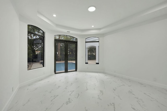 spare room featuring french doors, a raised ceiling, and baseboards