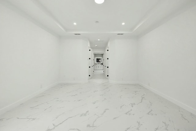 empty room featuring marble finish floor, baseboards, a raised ceiling, and recessed lighting