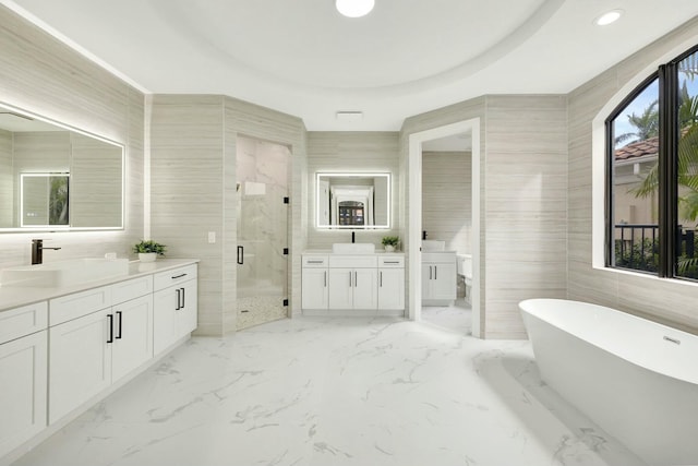 bathroom with a stall shower, two vanities, a sink, a freestanding bath, and tile walls