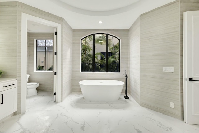 bathroom with marble finish floor, tile walls, a freestanding bath, toilet, and vanity