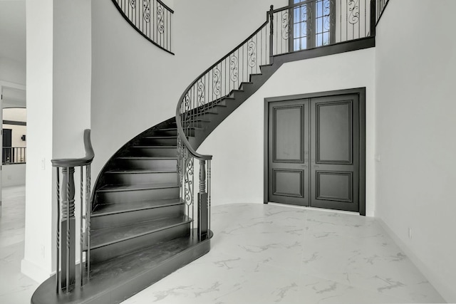 stairs featuring marble finish floor, a towering ceiling, and baseboards