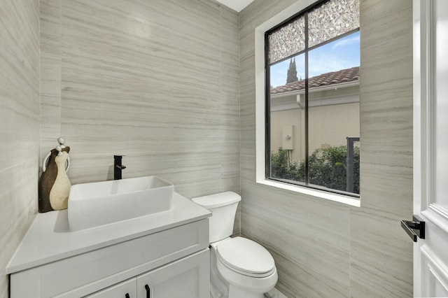 half bath featuring toilet, tile walls, and vanity