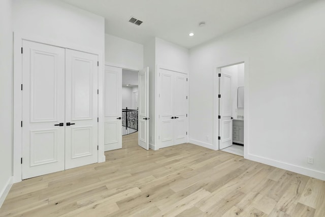 unfurnished bedroom with baseboards, light wood-style floors, visible vents, and multiple closets