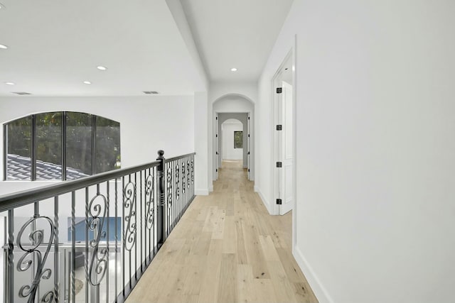 hallway featuring light wood finished floors, baseboards, visible vents, arched walkways, and recessed lighting