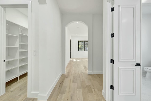 corridor with light wood-style flooring, arched walkways, and baseboards