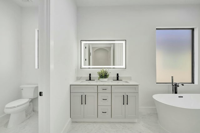 full bath with a sink, marble finish floor, a freestanding tub, and toilet