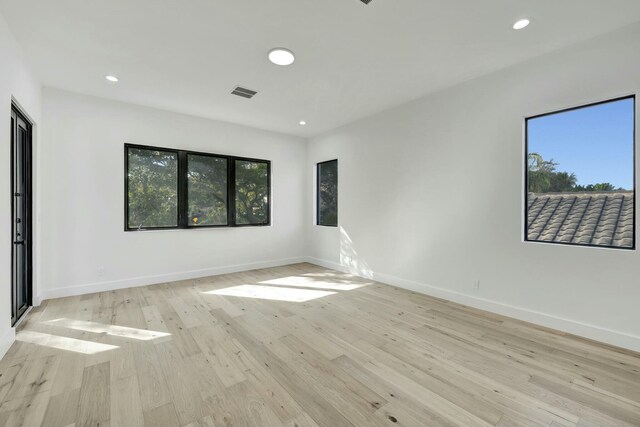 empty room featuring light wood-style floors, a wealth of natural light, visible vents, and baseboards