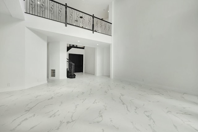 unfurnished living room featuring marble finish floor, baseboards, stairway, and a towering ceiling