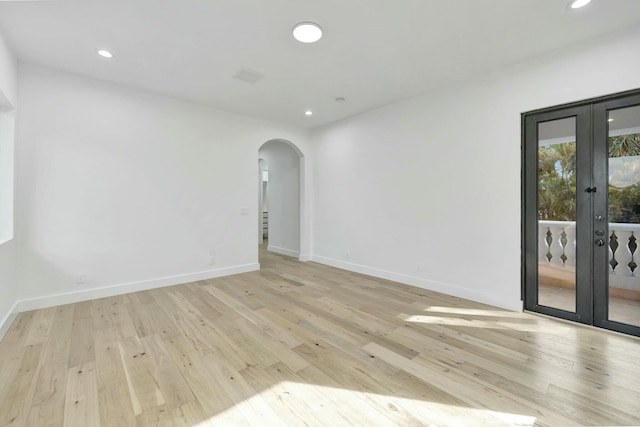 empty room featuring light wood-type flooring, arched walkways, and french doors