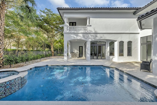 back of house featuring a patio, a balcony, fence, a pool with connected hot tub, and stucco siding