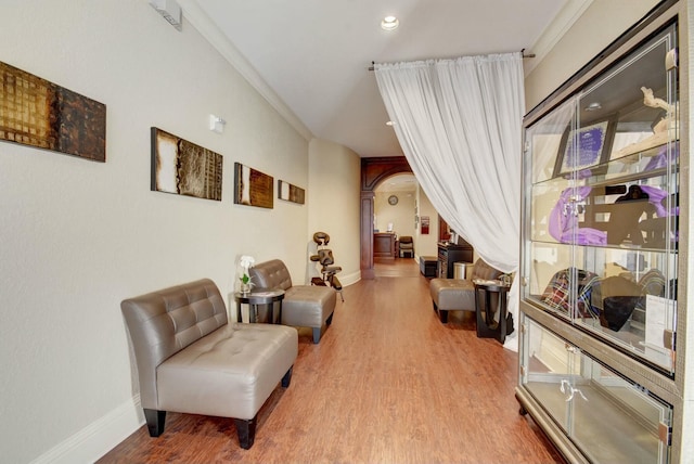 living area with baseboards, arched walkways, wood finished floors, and ornamental molding