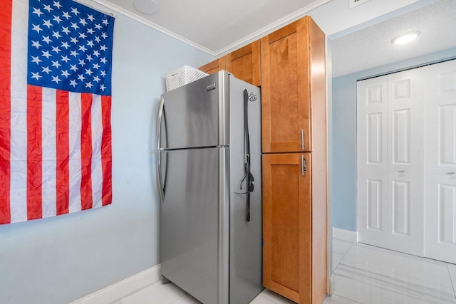 kitchen featuring light tile patterned floors, baseboards, brown cabinetry, and freestanding refrigerator