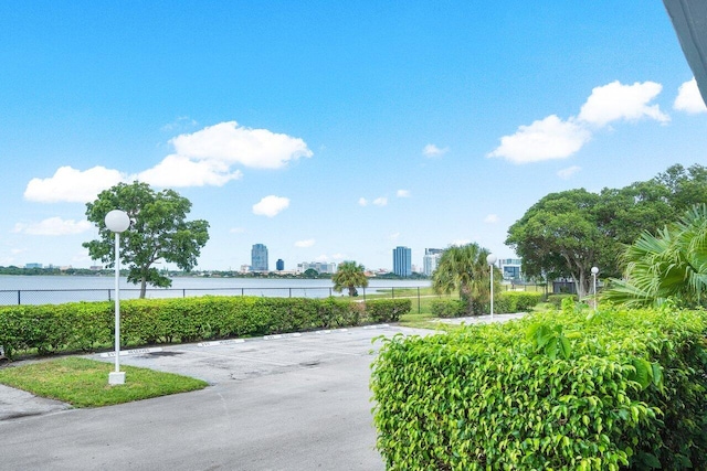 view of property's community featuring a water view, uncovered parking, fence, and a city view