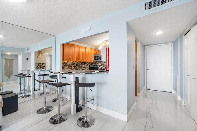 kitchen featuring a breakfast bar area, decorative backsplash, appliances with stainless steel finishes, a textured ceiling, and a peninsula