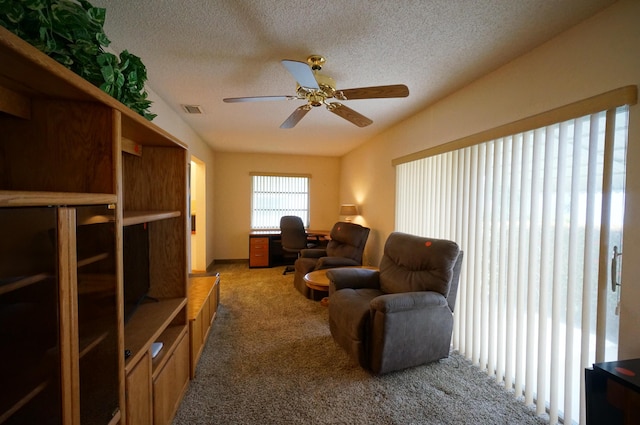 living area featuring a textured ceiling, carpet floors, visible vents, and a ceiling fan