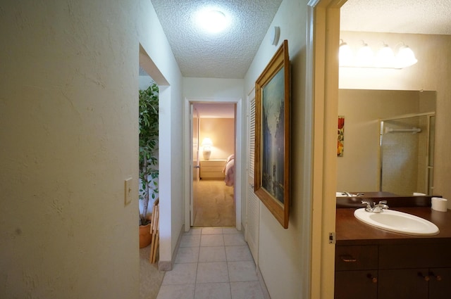 hallway featuring a textured wall, light tile patterned flooring, a sink, and a textured ceiling