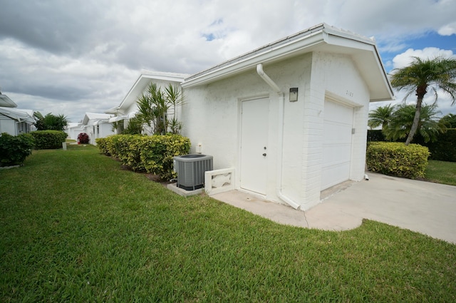 view of side of home with driveway, a lawn, an attached garage, central AC, and stucco siding