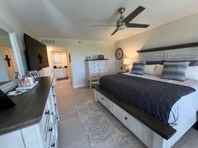 bedroom featuring light wood finished floors, visible vents, ceiling fan, a textured ceiling, and baseboards