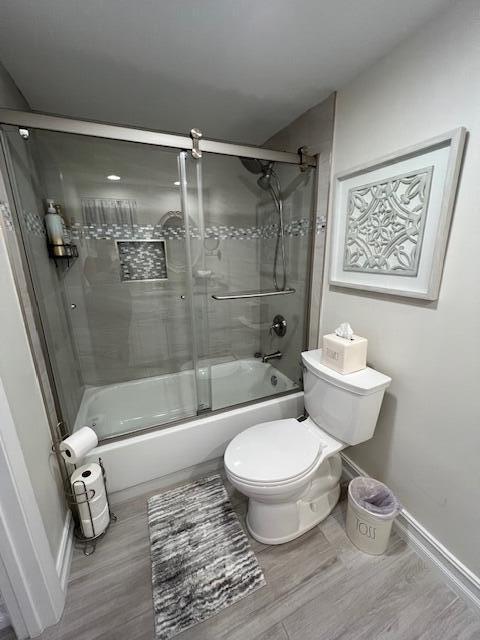 full bathroom with combined bath / shower with glass door, wood finished floors, toilet, and baseboards