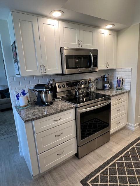 kitchen with light wood-style flooring, white cabinets, appliances with stainless steel finishes, tasteful backsplash, and dark stone countertops