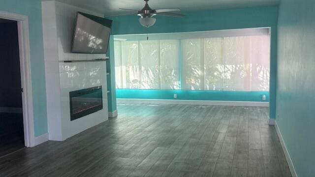 unfurnished living room with ceiling fan, baseboards, dark wood-style flooring, and a glass covered fireplace