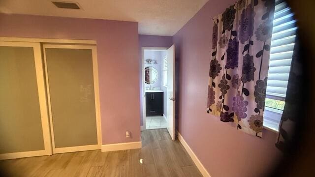 hallway with light wood-style floors, visible vents, and baseboards