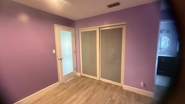 unfurnished bedroom featuring light wood finished floors, a closet, visible vents, and baseboards