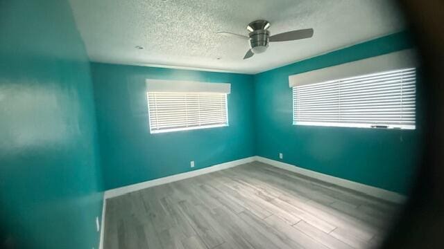 unfurnished room with a ceiling fan, a textured ceiling, baseboards, and wood finished floors