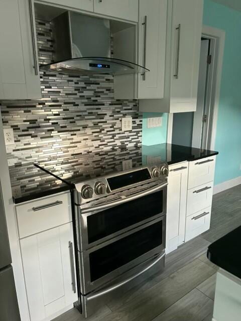 kitchen with dark countertops, wall chimney range hood, range with two ovens, and backsplash