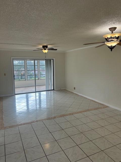 empty room with ceiling fan, light tile patterned floors, and a textured ceiling