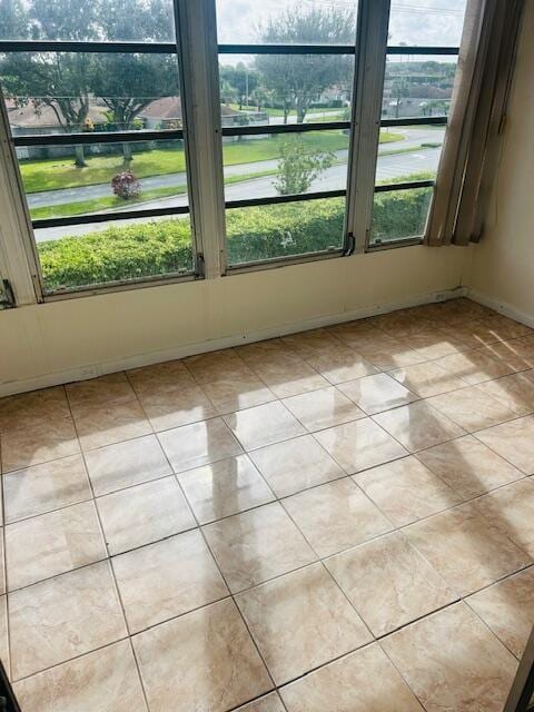 spare room with a water view, plenty of natural light, baseboards, and light tile patterned floors