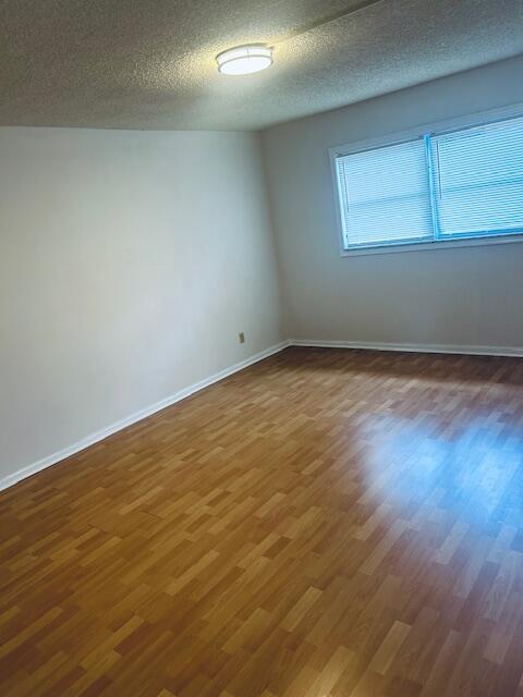 unfurnished room featuring a textured ceiling, baseboards, and wood finished floors