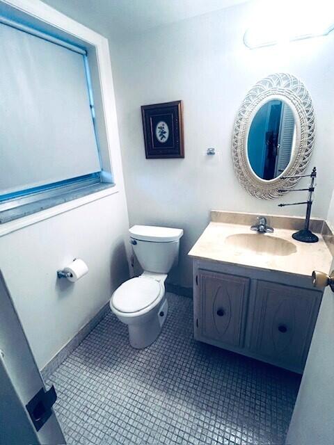 half bathroom with baseboards, vanity, toilet, and tile patterned floors