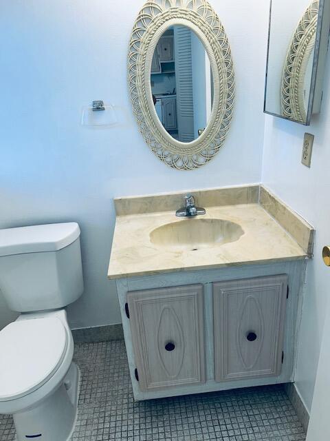 half bath with tile patterned flooring, baseboards, vanity, and toilet