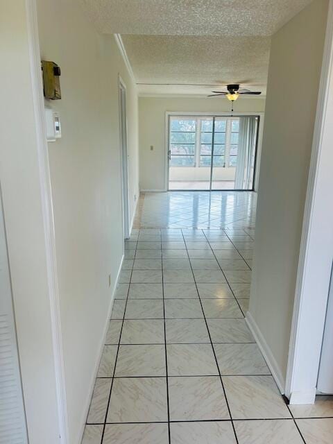 hallway with light tile patterned floors, baseboards, and a textured ceiling