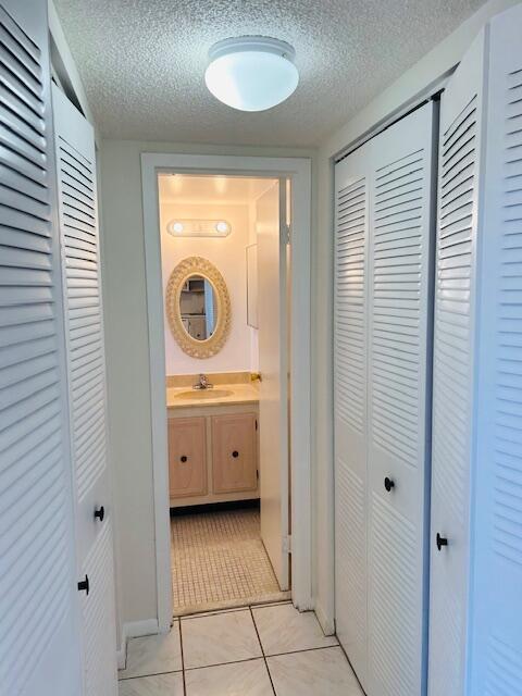 hall featuring a sink, a textured ceiling, and light tile patterned flooring