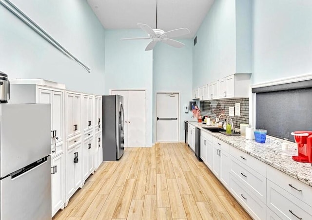 kitchen with light wood finished floors, stainless steel fridge, freestanding refrigerator, and white cabinetry