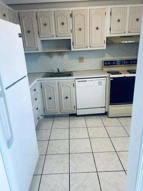 kitchen with light tile patterned floors, light countertops, a sink, white appliances, and under cabinet range hood