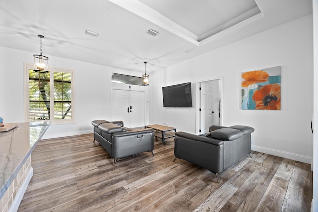 living area featuring a tray ceiling, baseboards, visible vents, and wood finished floors