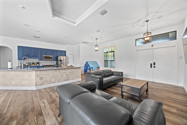 living area with arched walkways, visible vents, baseboards, and wood finished floors