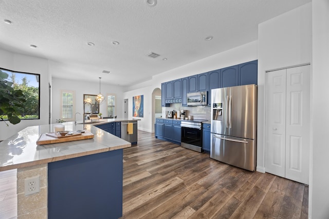 kitchen with arched walkways, a kitchen island with sink, blue cabinets, stainless steel appliances, and light countertops