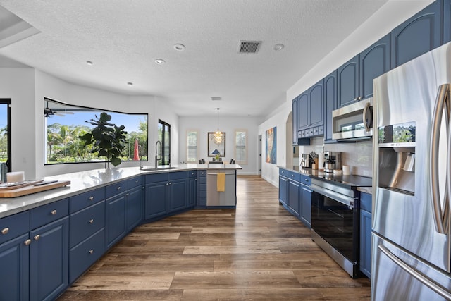 kitchen featuring decorative light fixtures, light countertops, stainless steel appliances, blue cabinetry, and a sink