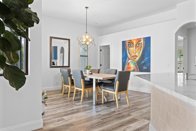 dining room with light wood-style floors, arched walkways, and baseboards