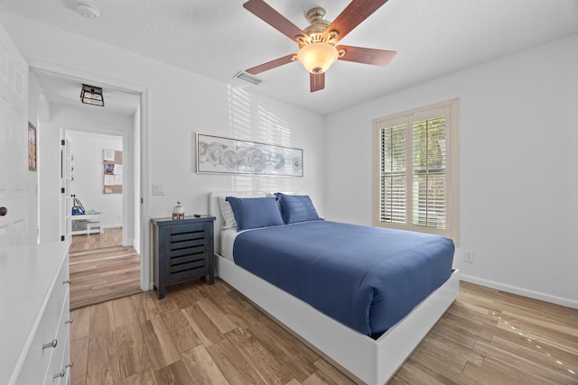 bedroom featuring baseboards, visible vents, ceiling fan, a textured ceiling, and light wood-style floors