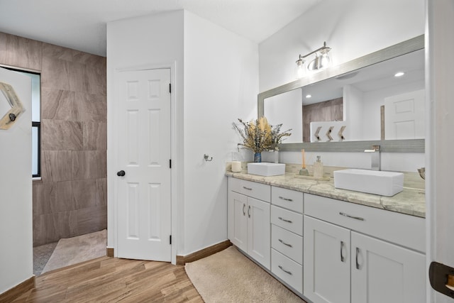 bathroom with wood finished floors, a sink, baseboards, and double vanity