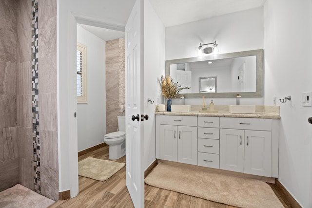 full bath with toilet, vanity, wood finished floors, tiled shower, and baseboards