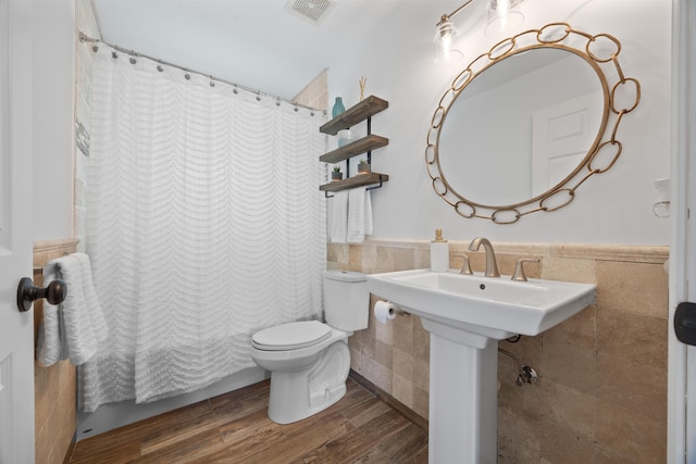 bathroom with a wainscoted wall, tile walls, visible vents, toilet, and wood finished floors