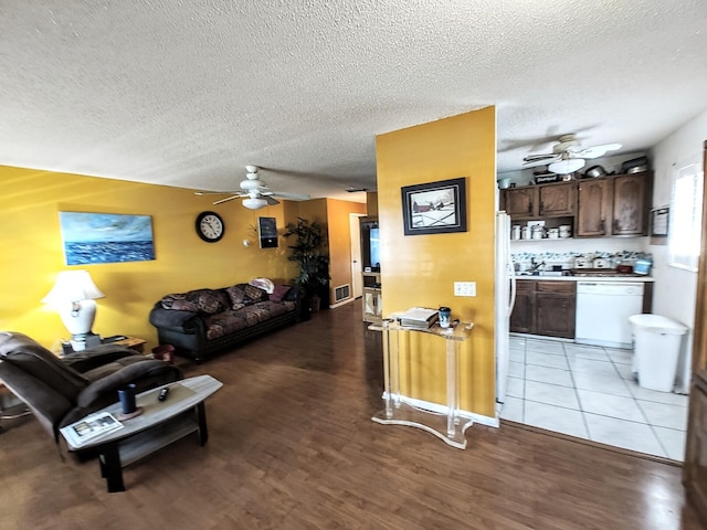 living room with light wood-style flooring, visible vents, ceiling fan, and a textured ceiling